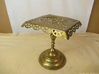 Side angle front view of the solid brass jardiniere stand showing the decorative pierced metal square top and rounded base.