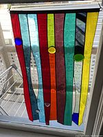 Full view of the stained glass window hanging showing colored vertical glass strips and round accent pieces.