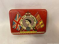 Top view of vintage red tin featuring Queen Elizabeth II portrait, crown, Union Jack and Canadian flags, and 'LONG MAY SHE REIGN' banner.
