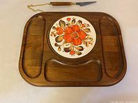 Top view of the vintage wooden cutting board with decorated ceramic inset and small knife laid above.