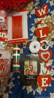 Photo showing a collection of Valentine's and holiday crafting supplies including a cupcake wreath, 'WELCOME' garland, ribbon spools, and crafting papers arranged on a floral tablecloth.