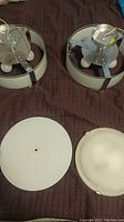 Two light fixtures and diffuser covers arranged on a surface showing housing, metal brackets, wiring terminals, and diffuser covers separately.