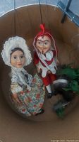 Female string puppet in floral dress with lace bonnet and male jester puppet in red and white with strings, displayed together