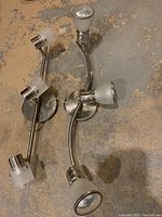 Photo showing two metal track light fixtures laid on a concrete floor, featuring curved arms and frosted glass shades on the light heads.