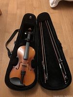 Top-down view of 3/4 violin in open case showing instrument body and two bows