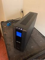 Front view of APC XS-100 UPS showing blue LCD screen with error code 'F01', power buttons, and APC logo.