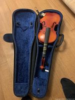 Full violin inside open case showing missing bridge and no strings, with chinrest attached, blue plush interior lining visible