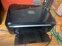 Black Canon MG6220 printer with paper trays extended positioned on a floor with cables around it