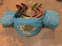 Photo of Puddle Jumper swim aid showing the blue arm floaties with turtle graphic and two sets of children’s bike training wheels with red and green wheels.