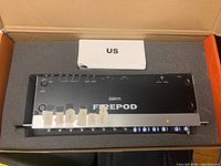 FirePod device oriented inside original foam packaging with white adapter box and labeled input jacks.