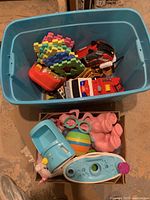 Blue storage bin containing assorted toys including colorful foam puzzle pieces, red toy vehicle, and plastic toys, not including toys outside the bin.