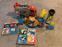 Photo showing orange and gray plastic truck and assorted plastic toys with board books next to them.