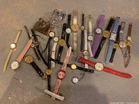 Photo showing approximately 33 assorted wristwatches arranged on a surface, including leather, metal, and plastic bands in various colors and styles.