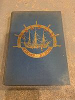 Front cover of blue cloth-bound Nelson Stamp Album with gold ship and helm emblem