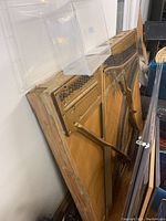 Photo of a large piano sound board still attached to the back frame of the piano, showing wooden structure, tuning pins, and strings.
