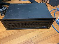 Front view of black rack mount amplifier with vented grille and QSC USA1310 branding