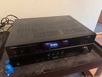 Front view of Yamaha RX-V667 receiver showing power on display with input HDMI1 and sound mode Drama.