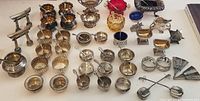 Front view of assortment of sterling silver open salt cellars, spoons, and decorative items