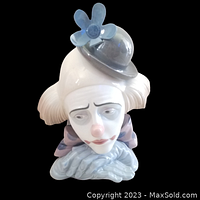 Front view of porcelain figure showing clown face with sad expression, grey hat with blue flower, pink bow tie, ruffled collar.