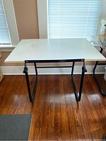Full front view of white drawing table with black metal legs, shows rectangular flat surface and sturdy frame.