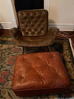 Front view of brown leather button tufted chair with matching ottoman in front, chair has one button missing.