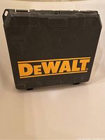 Front side of black DeWalt hard plastic tool case showing yellow DeWalt logo with two latches on top edge and slight surface scuffs