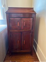 Closed view of the gramophone case cabinet showing the wood finish, four doors with wooden handles, and overall shape.
