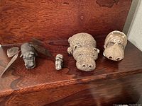 Photo showing 4 hippo items arranged on a wooden surface including metal winged hippo, small gray hippo, textured hippo, and ceramic planter hippo.
