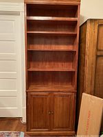 Front view of the solid wood bookshelf showing five open shelves and closed bottom cabinet with brass hardware.