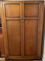 Front view of closed wooden antique armoire showing two paneled doors with round knobs and lock keyhole.