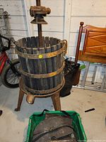 Full view of antique juice press showing wooden slat barrel, cast iron legs, and screw press mechanism on top