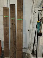 Three pieces of tall antique lumber leaning against a wall, showing rough wood surfaces and varying widths and tones.