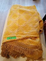 Full view of folded gold vintage bedspread showing fringe.