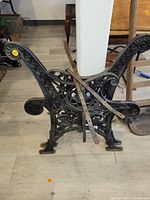 Side view of one cast iron bench end showing ornate scrollwork and curved armrest.