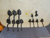 Seven vintage cast iron coat hooks with looped hooks and leaf-shaped backplates laid on a beige surface, showing rust and wear.
