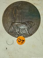 Full front view of circular bronze memorial plaque on white background with lot sticker