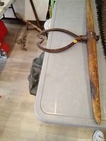 Full view of the antique wooden log carrier placed on a gray surface, showing the wooden handle and metal clamp with pointed ends for gripping logs.