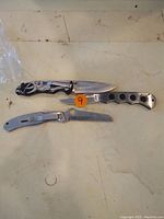 Three folding knives laid flat on a surface showing the entire length including handles and blades.