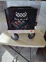 Aluminum dolly frame with a black plastic milk crate fitted on top. Shows how the dolly is designed to hold the crate securely.