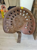 Front view of old rusted metal seat with oval ventilation holes and curved shape.
