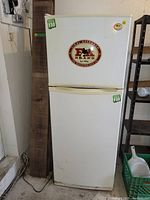 Full frontal view of the white LG apartment size fridge with top freezer, showing some stickers, scratches, and dirt on exterior.