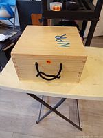 Closed wooden carrying case marked NPR with rope handles