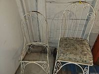 Two white metal garden chairs; one with floral cushion, one missing seat, with rust and wear visible