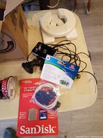 Photo showing SanDisk SD card 2-pack, black camera with cables and suction mount, and a white ceramic light fixture or cover.