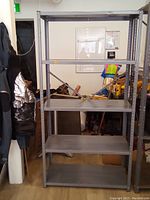 Full view of the four-shelf metal shelving unit standing on wooden floor with various items in background.
