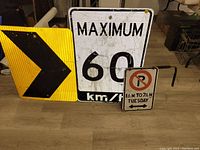 Three steel traffic signs side by side showing their fronts: maximum speed 60 km/h, yellow right arrow, and no parking time restriction sign.