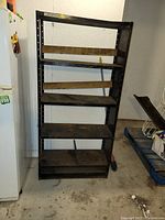 Front view of black steel shelving unit with wooden planks on shelves and visible wear including dents and rust marks.