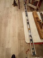 Full view of the 48-inch aluminum level tool lying on a white folding table next to two wooden hand planes and a small wooden ladder.