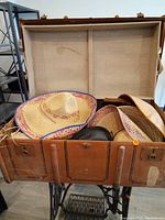 Open leather vintage trunk filled with various straw hats including a colorful sombrero style hat.