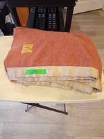 Folded vintage reddish-orange wool blanket with beige binding and green tape marked with number 39, placed on table.